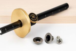 Brass wheel marking gauge with black graduated shaft, knurled brass knob, and replacement cutters displayed on a clean white surface with a light wood background.